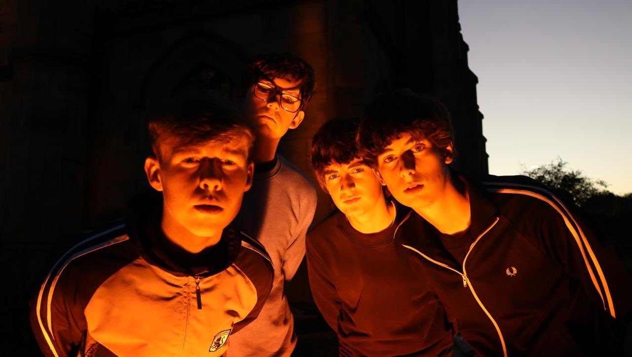 The Fleecers, Stockport indie rock band, photographed close together outside a church at dusk